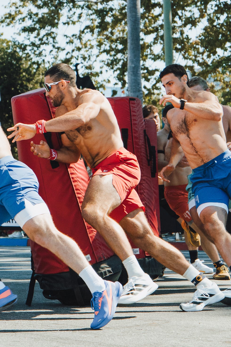 Athletes participating in a dynamic training drill, pushing against large padded obstacles outdoors.