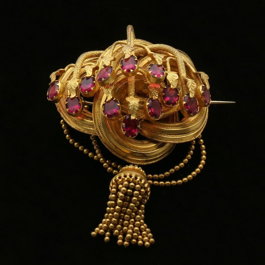 Gold jewelry with intricate design and ruby stones on a black background.