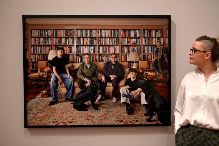 Two adult men and their teenage sons sitting on a sofa in a library.