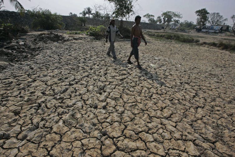 two people walk across cracked dry soil