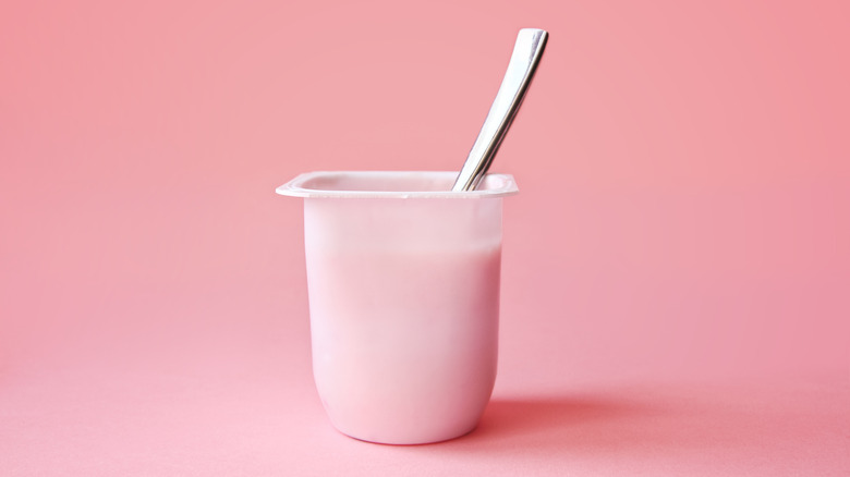 pink yogurt container with spoon on pink background