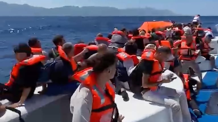 In this frame grab from a video, passengers wearing life jackets wait atop a capsized passenger vessel to be rescued off the coast of Girne.