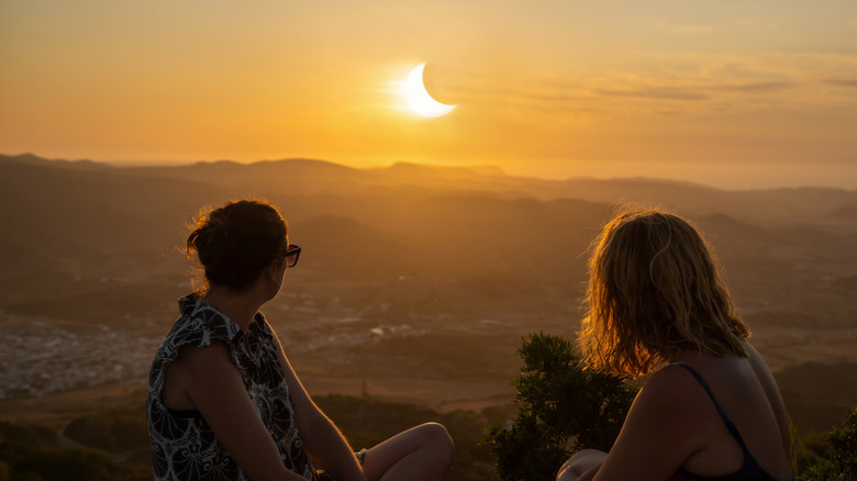 Two women looking at a partial eclipse in the sky