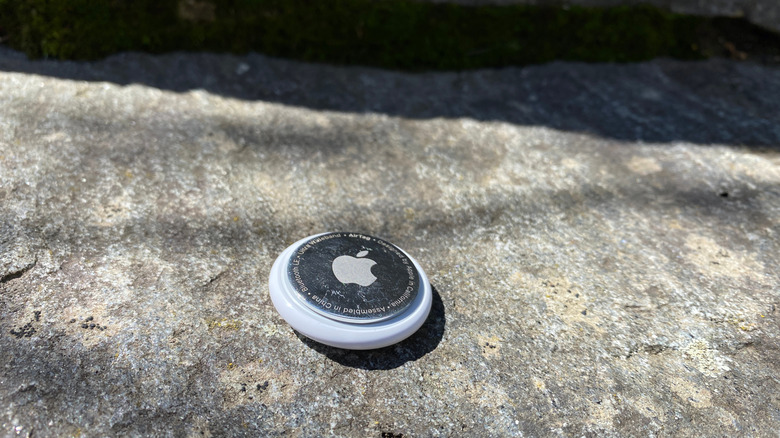 An AirTag sitting on a rock outside.