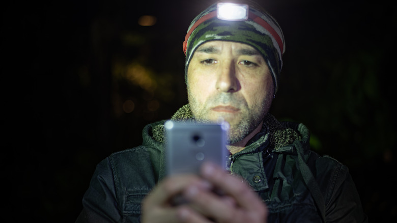A man looking at his phone in the dark with a torchlight on his cap