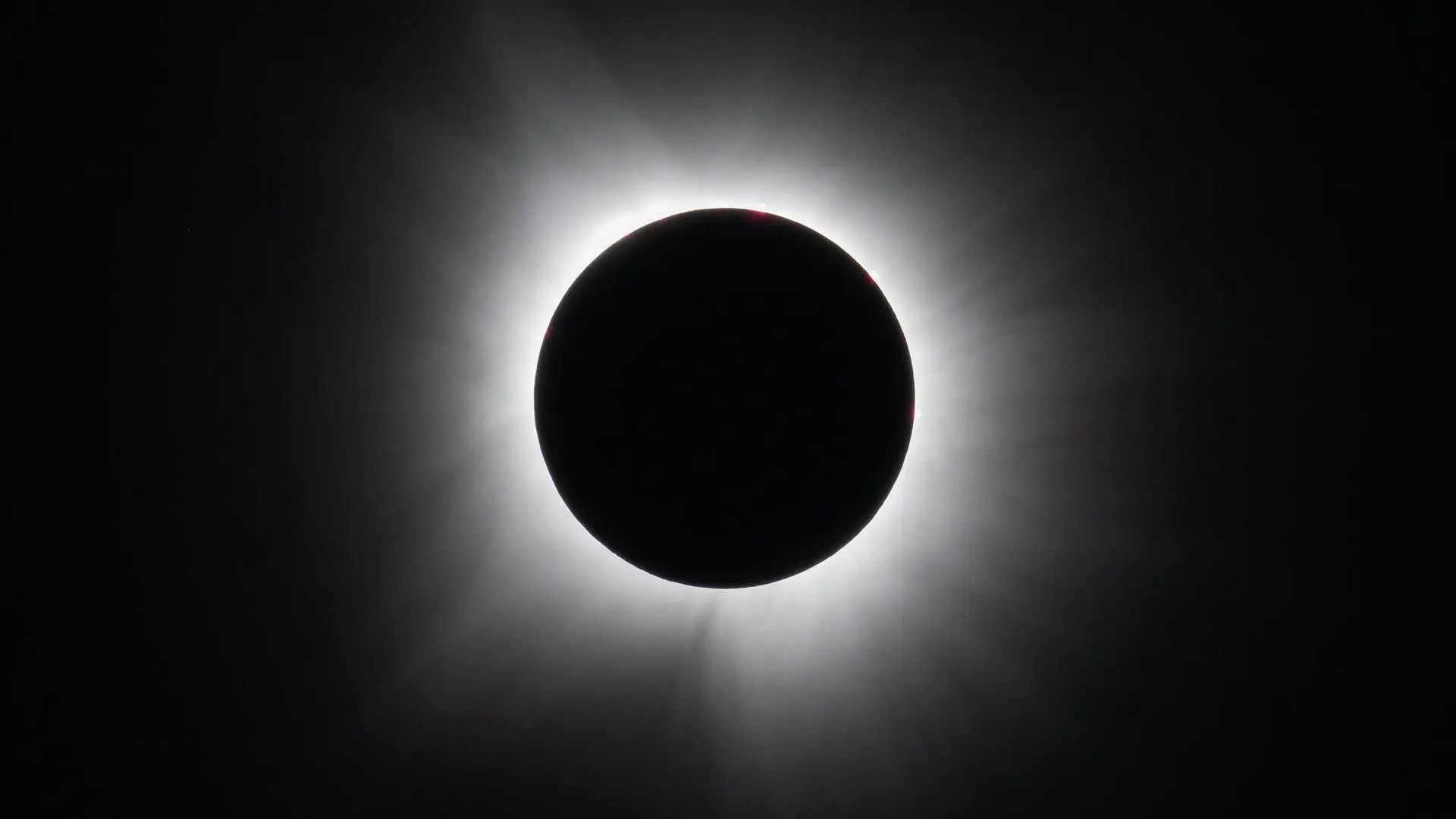 A black circle against a black background surrounded by white wispy tendrils
