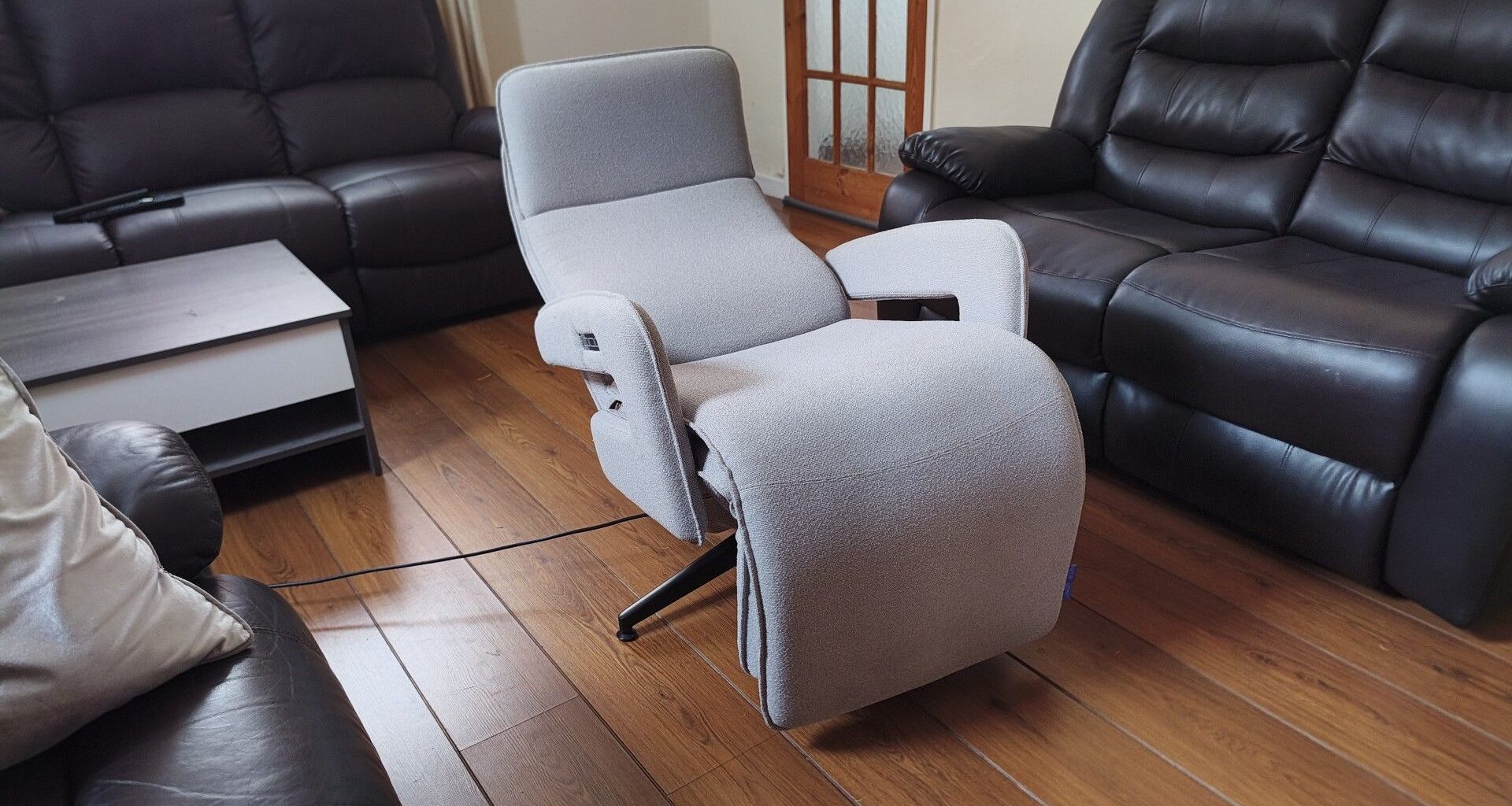 Side view of the recliner fully reclined into its flat position, with its black swivel base visible on the wooden floor.