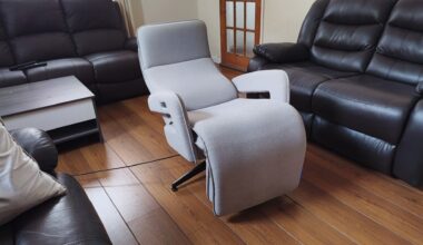 Side view of the recliner fully reclined into its flat position, with its black swivel base visible on the wooden floor.