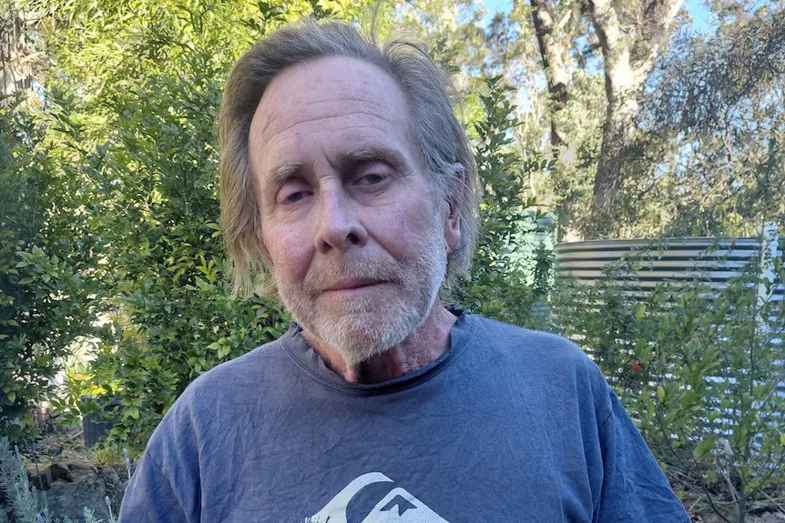 An older man looks into the camera, looking displeased