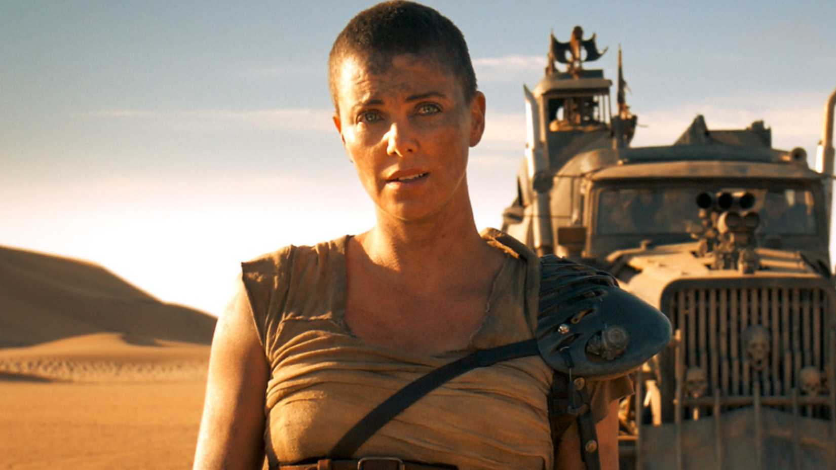 Charlize Theron as Furiosa in Mad Max Fury Road with a large truck behind her