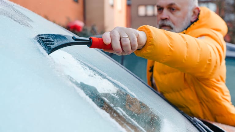 man scrapes ice off his car windshield