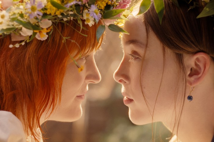 monster-lizzie-borden-ella-vicky Vicky Krieps and Ella Beatty sat staring at each other, with their faces close together, wearing floral crowns.