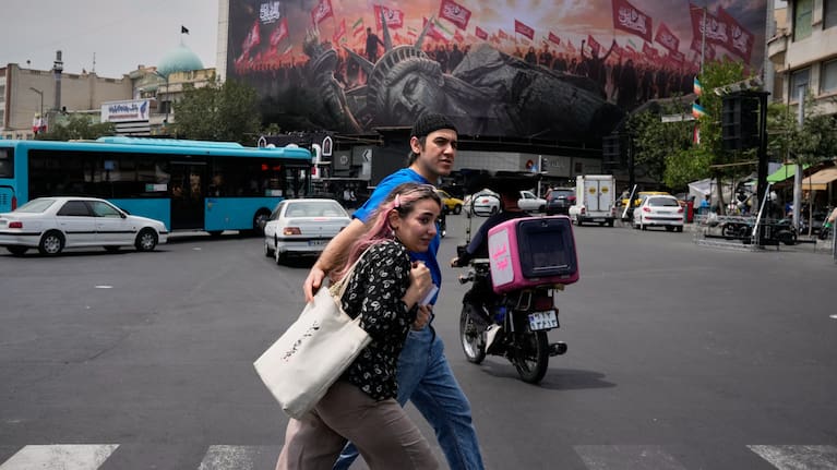 Pedestrians cross a street in front of a billboard depicting a fallen Statue of Liberty and crowds carrying Iranian and Shiite flags at Revolution Square in Tehran, Iran.