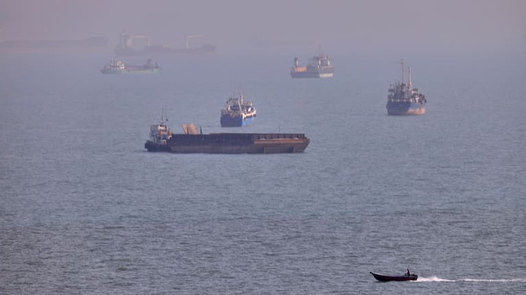 People spend time at a beach as commercial vessels are anchored in the Strait of Hormuz off Bandar Abbas, Iran,