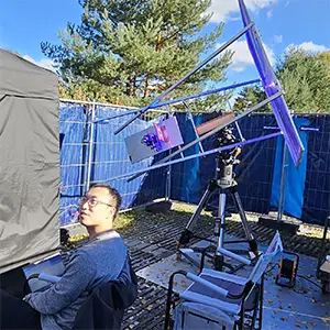 Cheng Li is shown with the outdoor experimental setup. The sunlight concentration module, including the Fresnel lens and the solar concentrator, is mounted on a solar-tracking motor to ensure stable power delivery. The entanglement generation and detection setup, including the nonlinear crystal and the single-photon detectors, are shielded in an optical enclosure placed inside a blackout tent. Credit: Jasvinder Brar, Max Planck Institute for the Science of Light