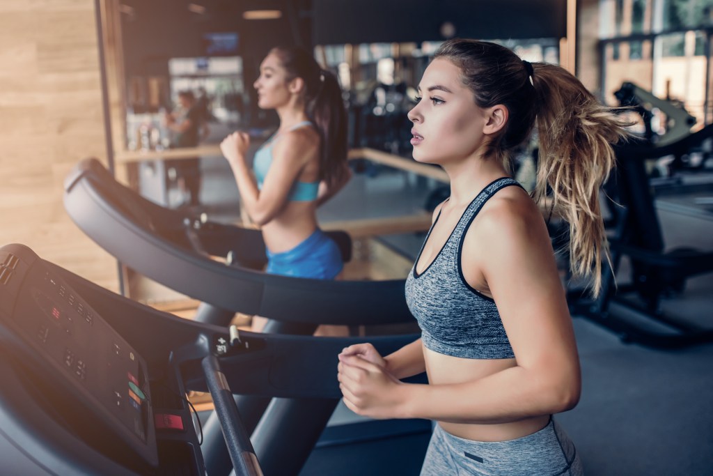 Two women run on treadmills at a gym.