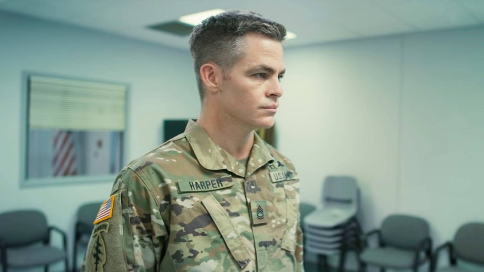 Chris Pine stands in an office room in uniform in The Contractor