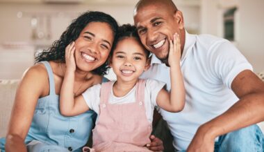 Three people together smiling while the middle one has hands on the others' faces.
