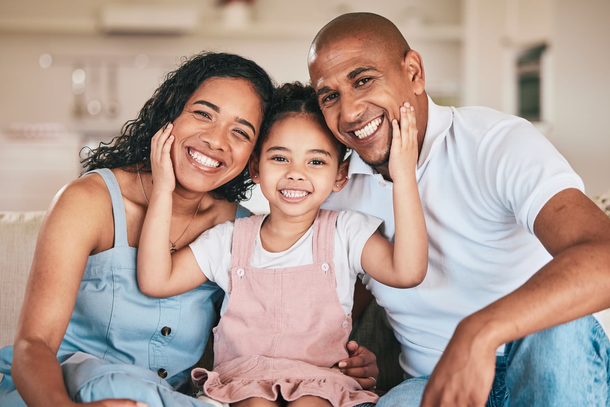 Three people together smiling while the middle one has hands on the others' faces.