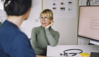 Patient leaning on elbow while discussing with nurse during visit at hospital.