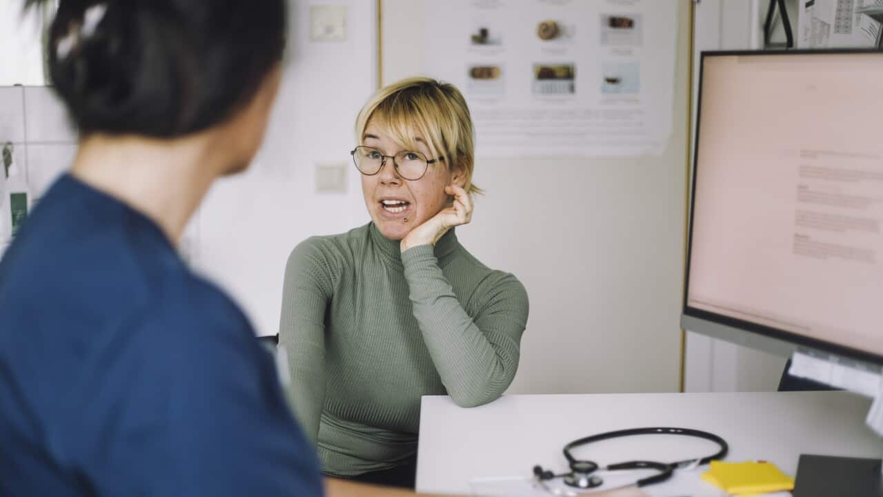 Patient leaning on elbow while discussing with nurse during visit at hospital.