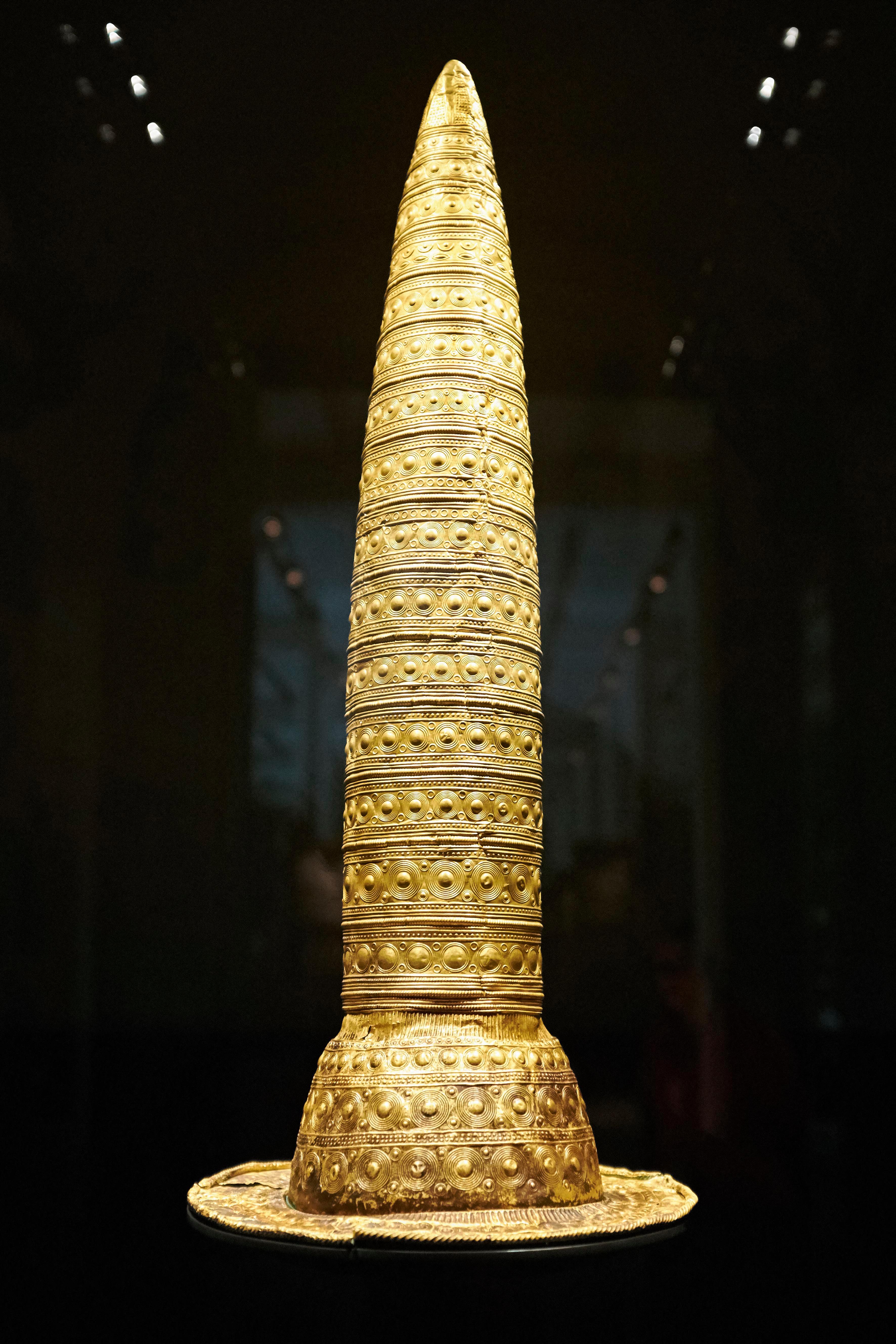 a conical gold hat on display with a black background