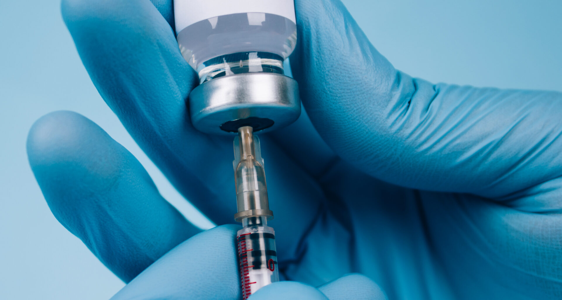 Blue-gloved hands using a needle and bottle to give a vaccine.