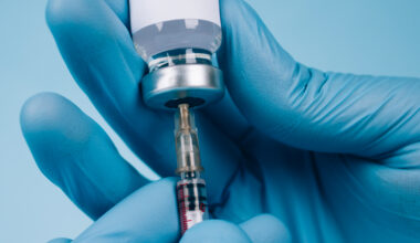 Blue-gloved hands using a needle and bottle to give a vaccine.