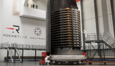 A stack of thin satellites sits in half a rocket fairing in a clean room.