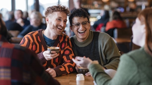 Group of friends sitting in a cafe enjoying a hot drinks together. They are talking, sitting at a table with a view in Tynemouth, North East of England. They are two couples, double dating. One of the couples are LGBTQI+.