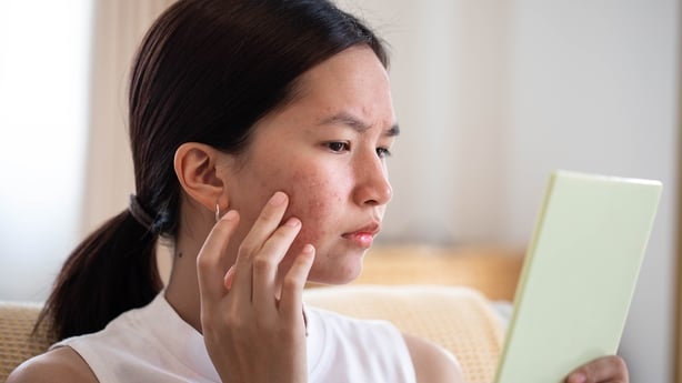 Portrait of Asian woman worry about her face when she saw the problem of acne inflammation and scar by the mini mirror.