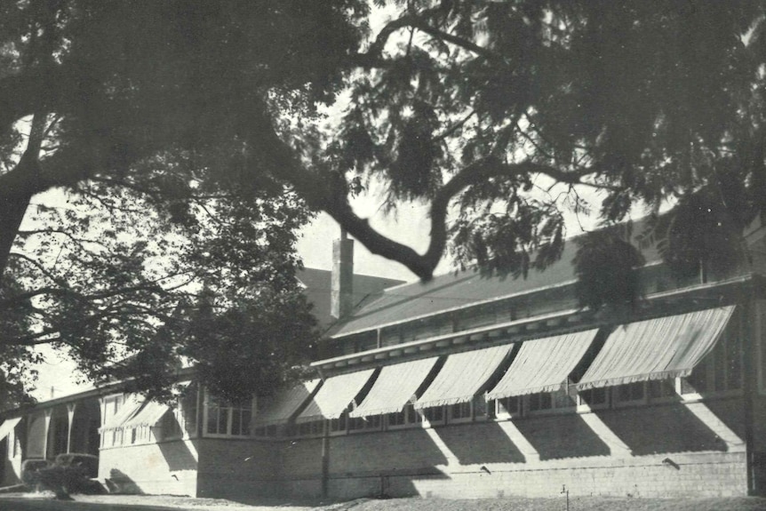 A black and white photo depicting a series of three multi-storey brick buildings next to a road.