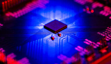 Close-up of a microchip on a circuit board lit in blue and red.