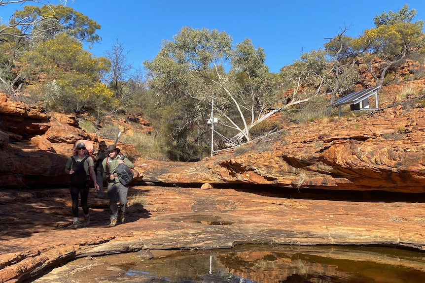 A woman and a man in outdoor gear on the rocky edge of an outback waterhole.