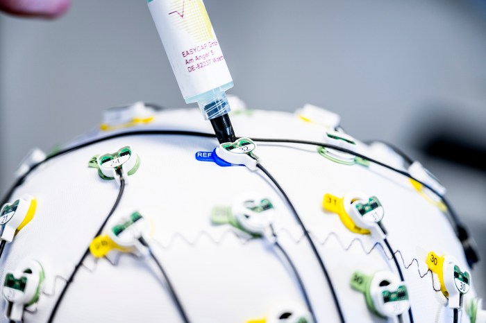 Close-up of numbered EEG electrodes clipped into the cap, with a syringe applying gel to one sensor.