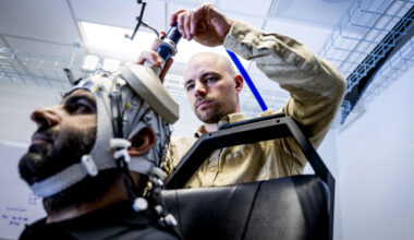 Sherman adjusts an EEG electrode on a cap fitted to a study participant's head, shot from a low angle with a tangle of colored wires visible against the cap.