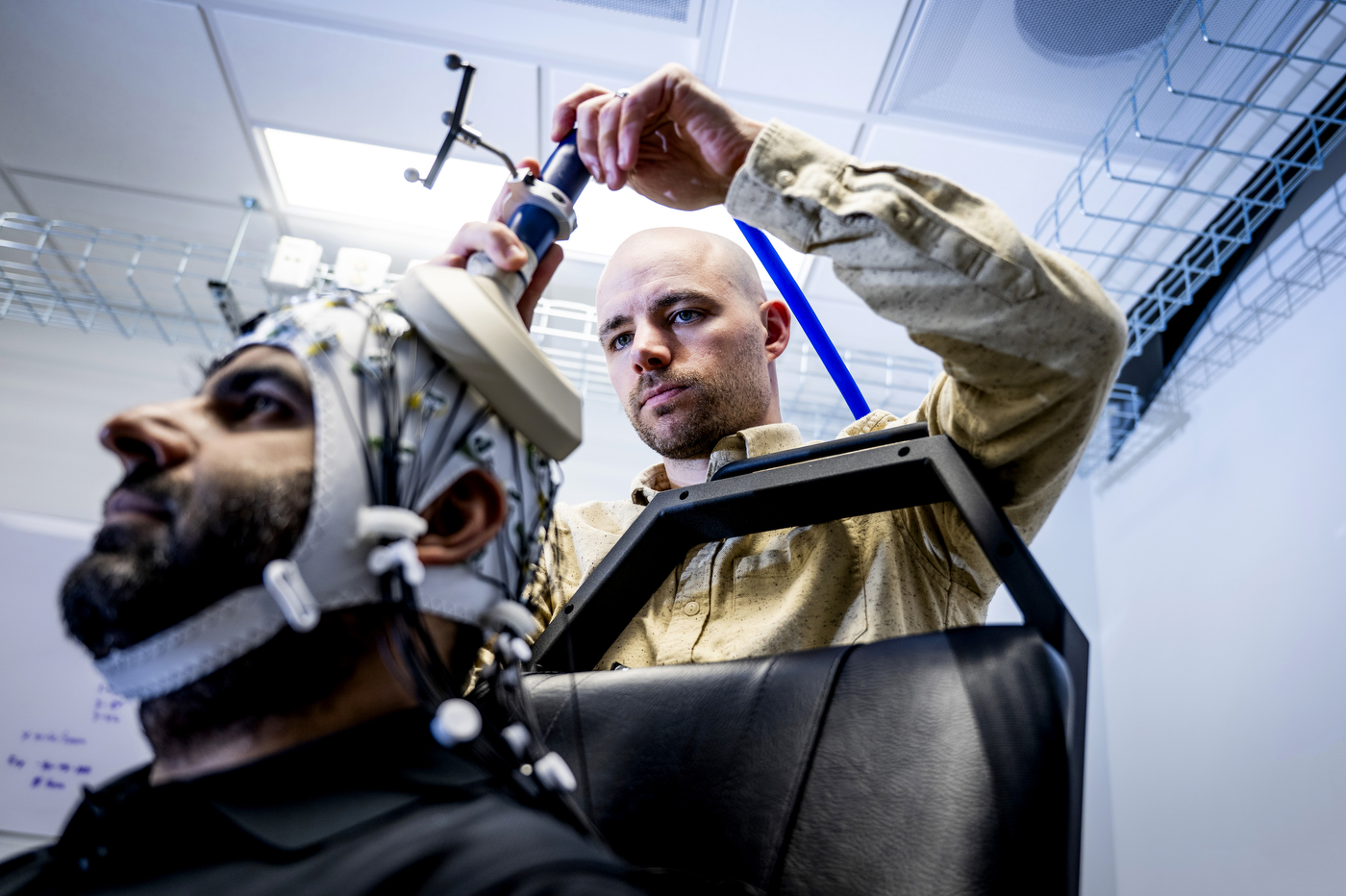 Sherman adjusts an EEG electrode on a cap fitted to a study participant's head, shot from a low angle with a tangle of colored wires visible against the cap.