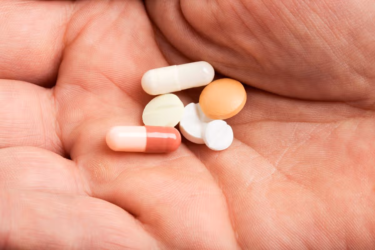 daily dose of medicine - various pills, tablets and capsules on the palm of a male hand