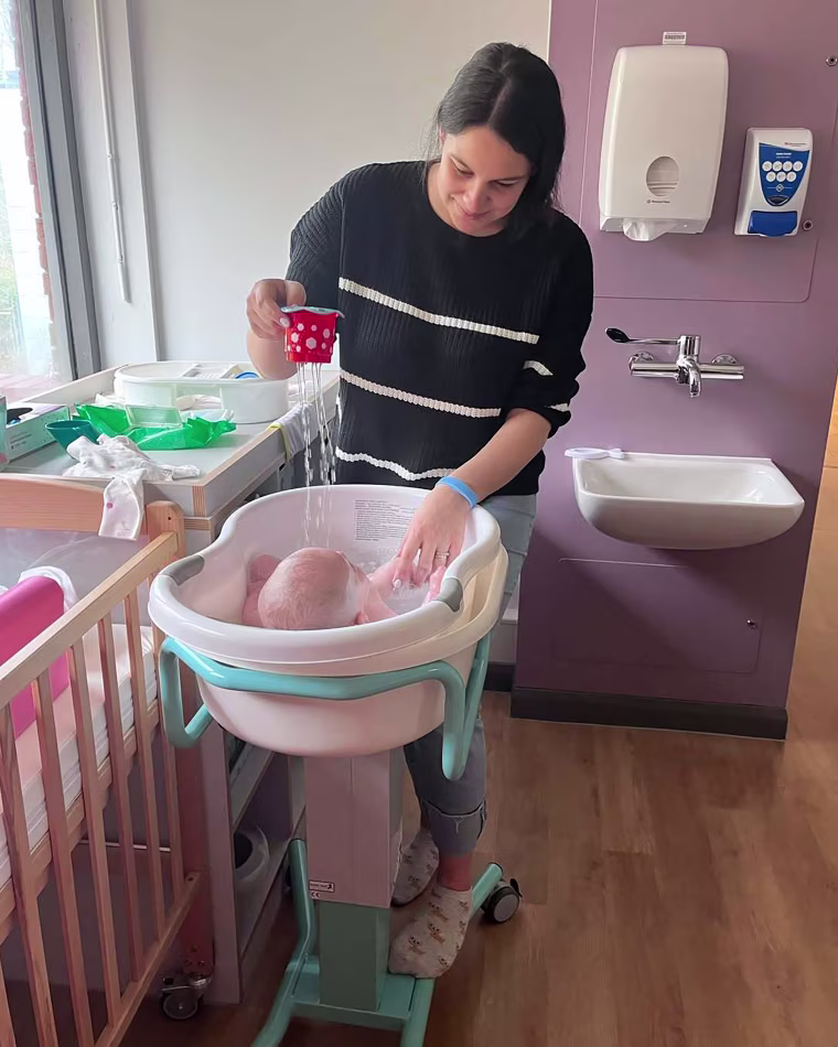 Image: Sofii Lewis bathes her daughter Evie in a small plastic baby bathtub, in a mother and baby hospital unit