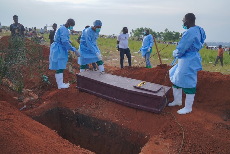 People dressed in protective gear prepare to lower a coffin.