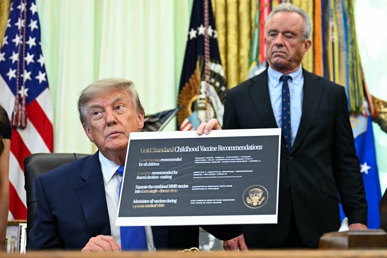 Donald Trump, left, sits at his desk in the Oval Office. He holds a sign with the headline "Gold Standard Childhood Vaccine Recommendations." Robert F. Kennedy Jr. stands, out of focus, behind him.
