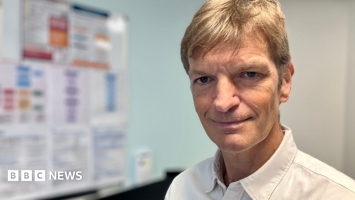 A man in a white shirt in a GP consulting room