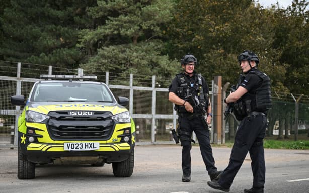 Armed police stand guard manning a roadblock at an entrance to RAF Fairford base in Fairford, south-west England on September 27, 2026, as UK counter-terrorism police investigate an incident near the base in the village of Whelford. British police on September 27 declared a major incident and evacuated villagers living near a base used by the US air force after arresting several men on suspicion of explosives offences. (Photo by JUSTIN TALLIS / AFP)
