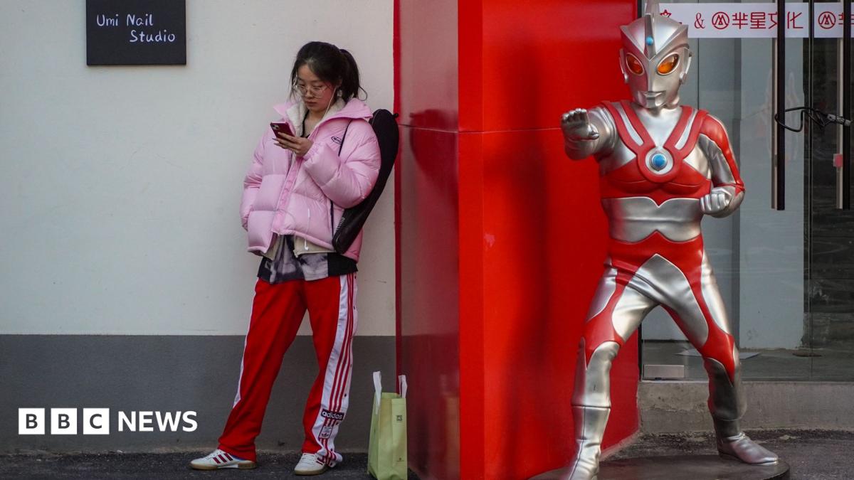 A young woman stands beside a life-sized Ultraman statue outside a shop.