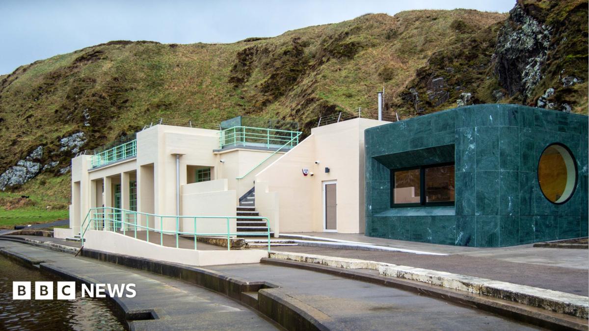 Tarlair Pool Pavilion, a restored Art Deco building beside the seawater pool, featuring cream-coloured walls, pale green railings, rooftop terraces, and a modern dark green extension, set against a rugged coastal hillside.