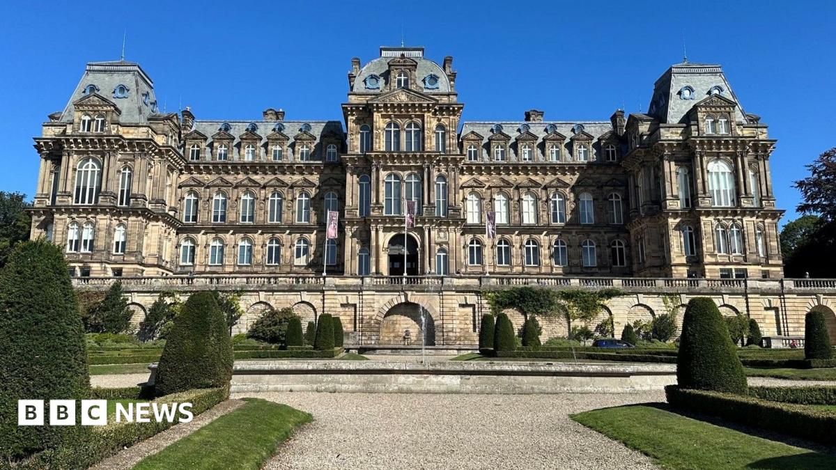 A large building in the French Renaissance style of architecture - four storeys with large windows, projecting bays, and mansard roofing. Stairs on either side lead up the the central entrance. In front is a formal garden with a wide gravel path, patches of lawn, and clips shrubbery.