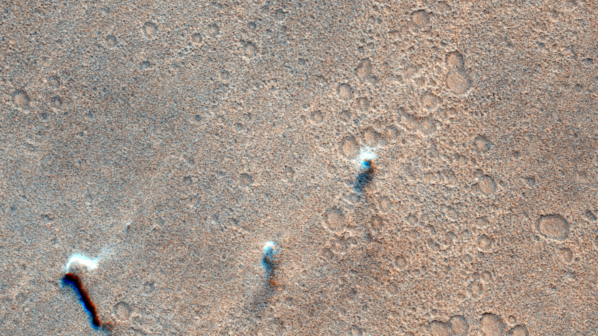 satellite photo of three dust devils on mars, showing them as three whitish puffs against a cratered, reddish-brown landscape