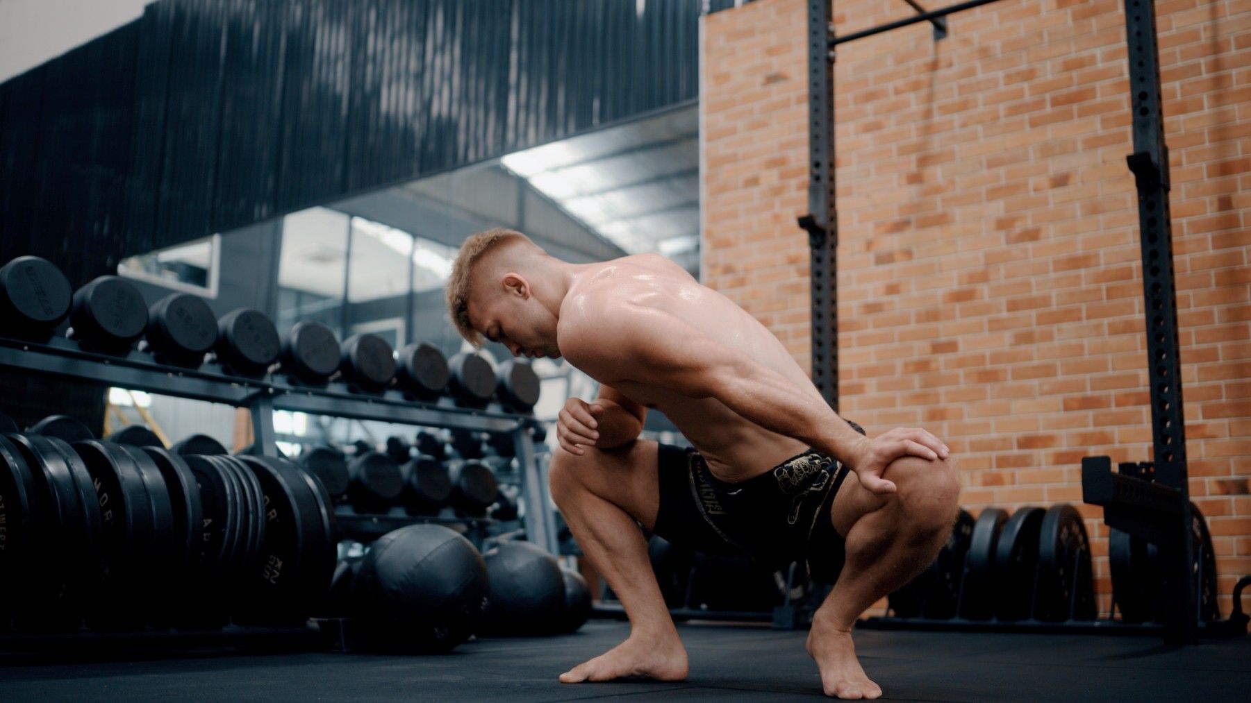 Athletic male in shorts at the gym performing a low squat hold while stretching out his hips