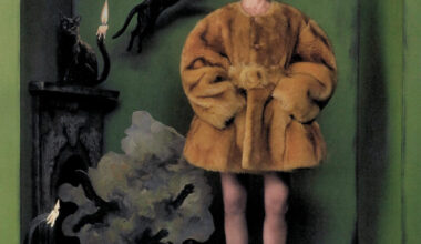 Sandra Bullock stands before a green wall with her feet turned outward and hands in the pockets of a fur coat. She is surrounded by cut-outs of black cats.
