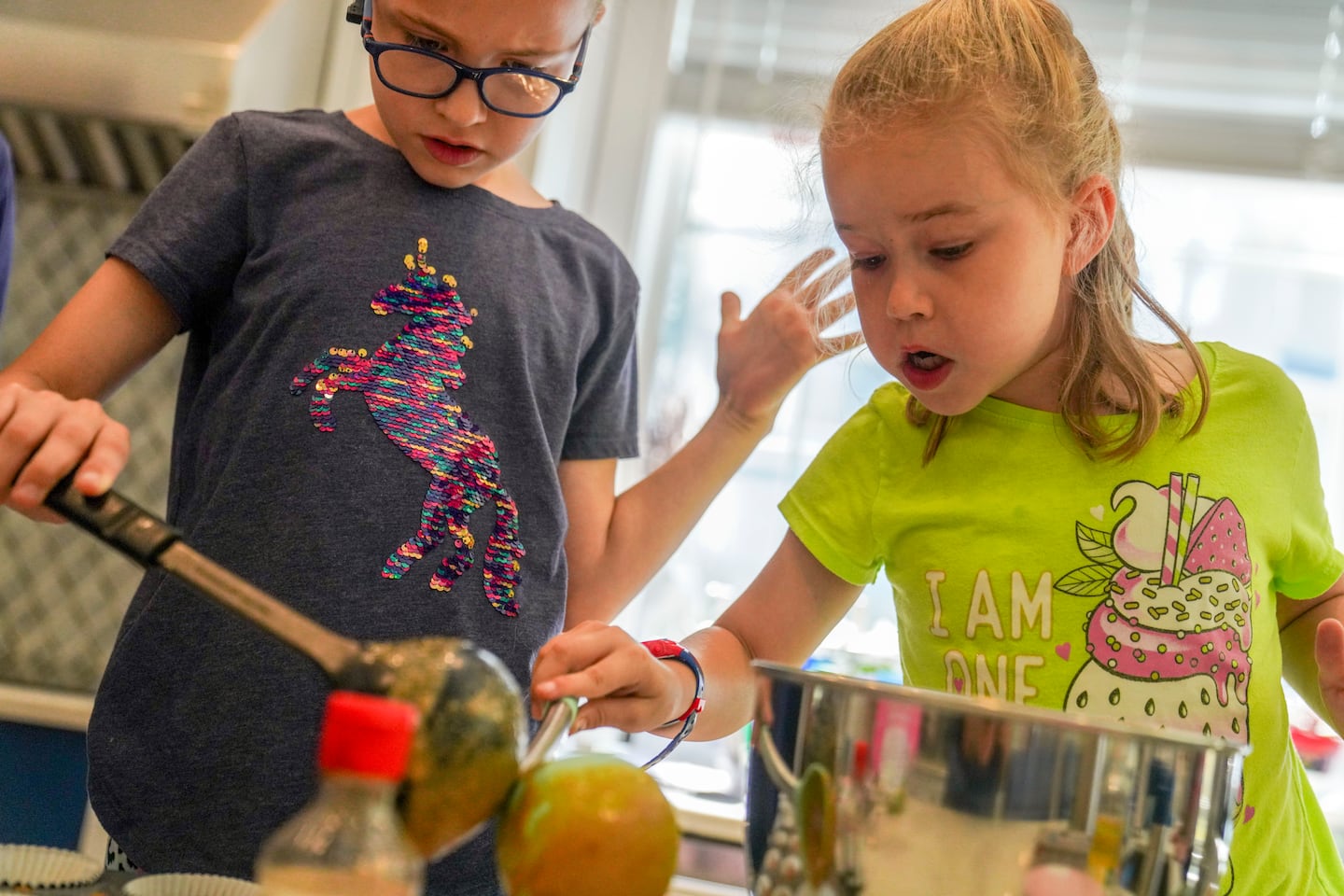 Fiona and Olivia transferred cupcake batter into the pan in their kitchen.